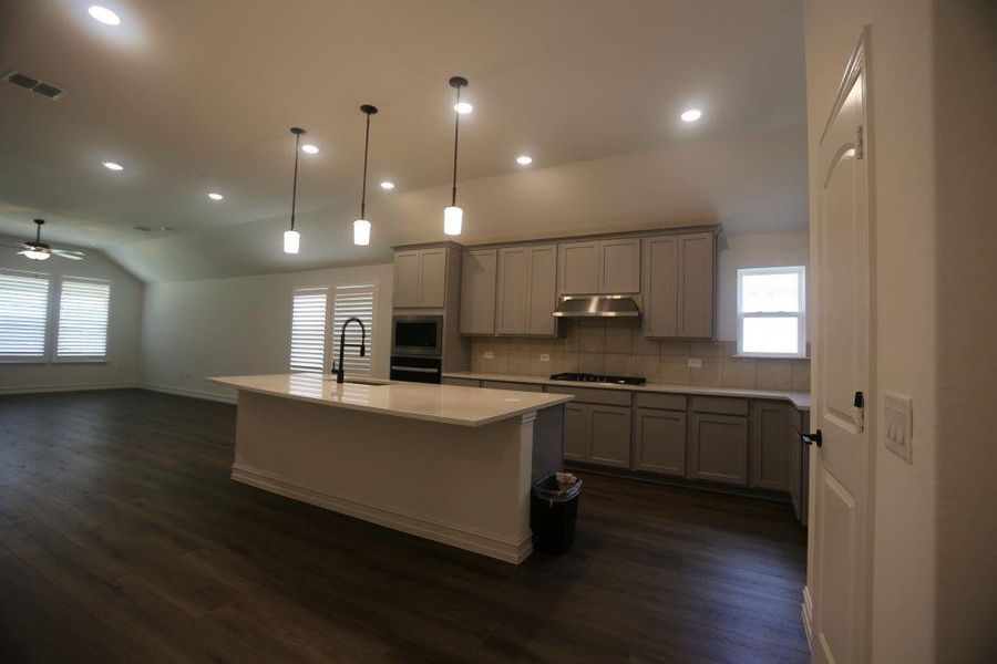 Kitchen island with a matte black gooseneck faucet and three pendant lights, complemented by recessed lighting