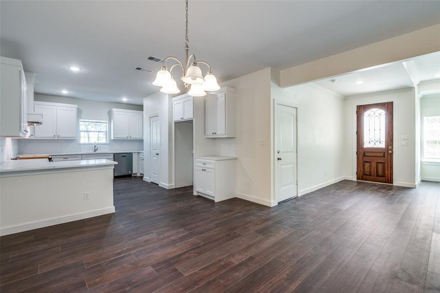 Kitchen featuring dark wood-type flooring, pendant lighting, an inviting chandelier, stainless steel dishwasher, and white cabinets