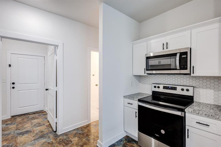 Kitchen with white cabinetry, tasteful backsplash, stainless steel appliances, light stone counters, and dark tile patterned flooring