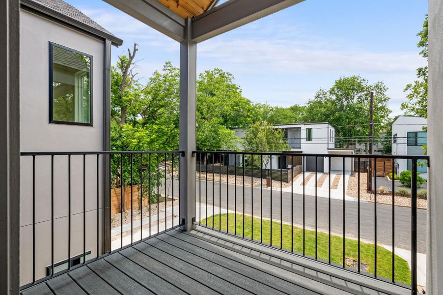 A private balcony offers a vantage point over the neighborhood street and lush green trees.