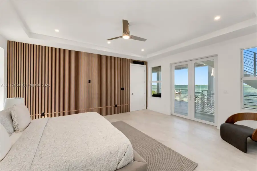 Slatted wood-finish accent wall, tray ceiling with recessed lighting, light-toned wood-finish flooring, and glass French doors leading to an exterior balcony Slatted wood-finish accent wall, tray ceiling with recessed lighting, light-toned wood-finish flooring, and glass French doors leading to an exterior balcony