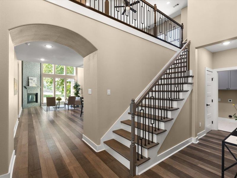Stairway with arched walkways, hardwood / wood-style floors, recessed lighting, a high ceiling, and a fireplace