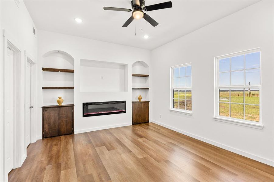 Spacious room featuring wood-finish flooring, an electric fireplace with an integrated media niche, built-in shelving with arched alcoves, and two double-hung windows