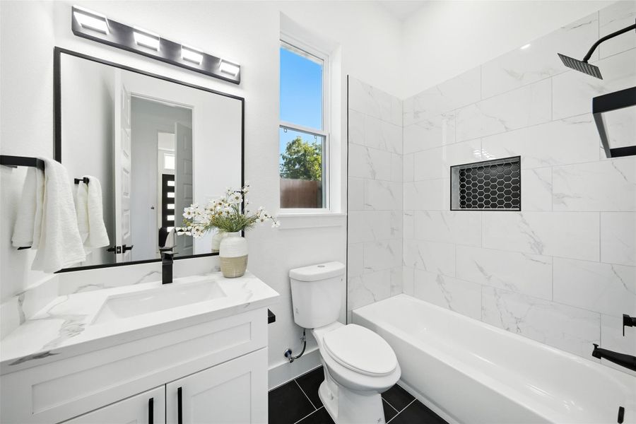 Modern, first floor full bathroom with clean, contemporary finishes, featuring a Quartz vanity, sleek black fixtures, and a large framed mirror with updated lighting. The shower/tub combo showcases designer tile with a built-in niche, while a window brings in natural light—perfect blend of style and functionality. Modern, first floor full bathroom with clean, contemporary finishes, featuring a Quartz vanity, sleek black fixtures, and a large framed mirror with updated lighting. The shower/tub combo showcases designer tile with a built-in niche, while a window brings in natural light—perfect blend of style and functionality.