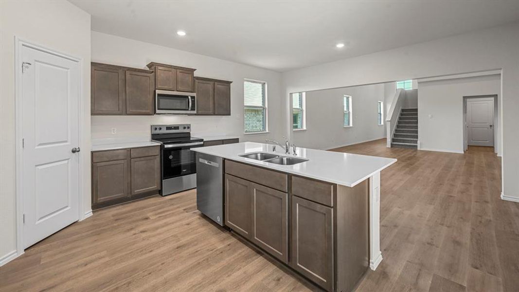 Kitchen featuring a central island with dual sinks, light-toned countertops, wood-finish flooring, stainless steel appliances, and gray cabinetry