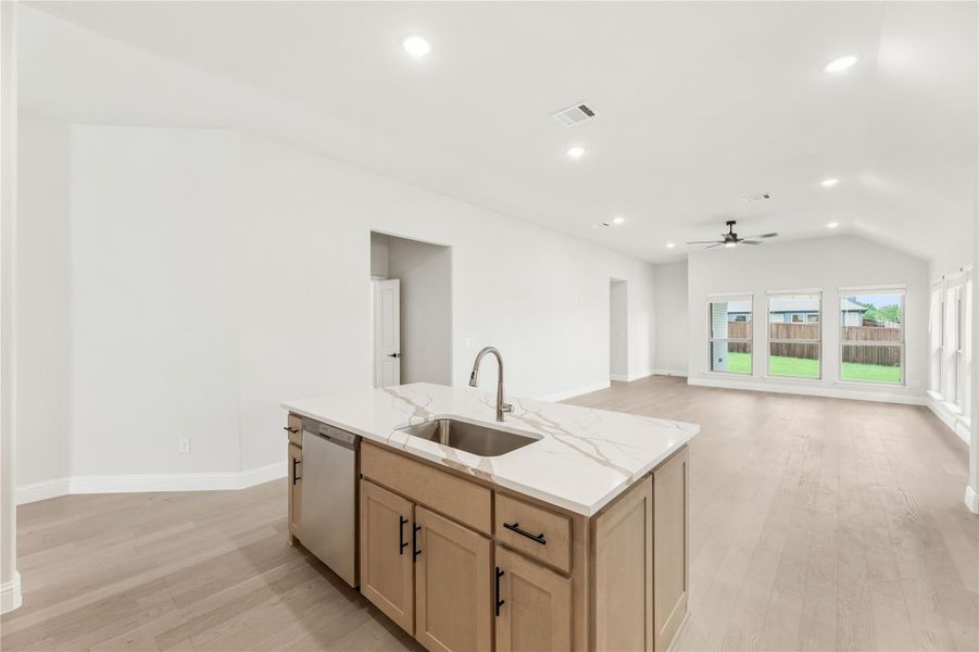 Kitchen island with quartz countertop and sink, open to living area with light wood floors and ceiling fan.