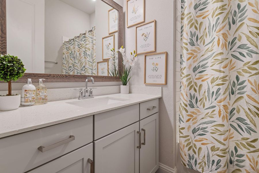 Bright, modern bathroom with a sleek white countertop and vanity. Features a large mirror with a wood frame, decorative plants, and art. A shower curtain with a botanical design adds a touch of nature. Bright, modern bathroom with a sleek white countertop and vanity. Features a large mirror with a wood frame, decorative plants, and art. A shower curtain with a botanical design adds a touch of nature.