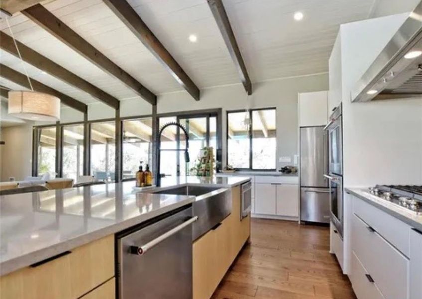 Kitchen featuring modern cabinets, light wood finished floors, wall chimney range hood, appliances with stainless steel finishes, and light stone countertops Kitchen featuring modern cabinets, light wood finished floors, wall chimney range hood, appliances with stainless steel finishes, and light stone countertops