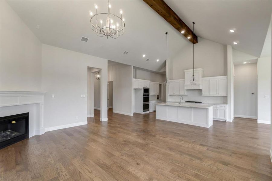 Unfurnished living room featuring an inviting chandelier, beamed ceiling, hardwood / wood-style floors, sink, and high vaulted ceiling