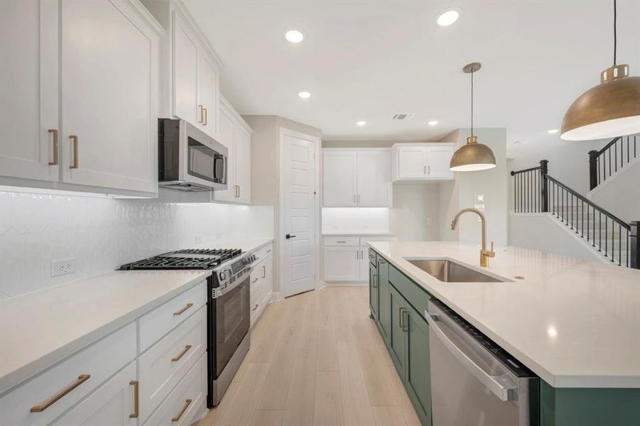 Kitchen featuring two tone cabinetry, stainless steel appliances, a center island with sink, light stone counters, and light wood finished floors
