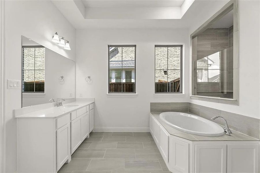 Bathroom with a tray ceiling, tile patterned floors, vanity, and a bath