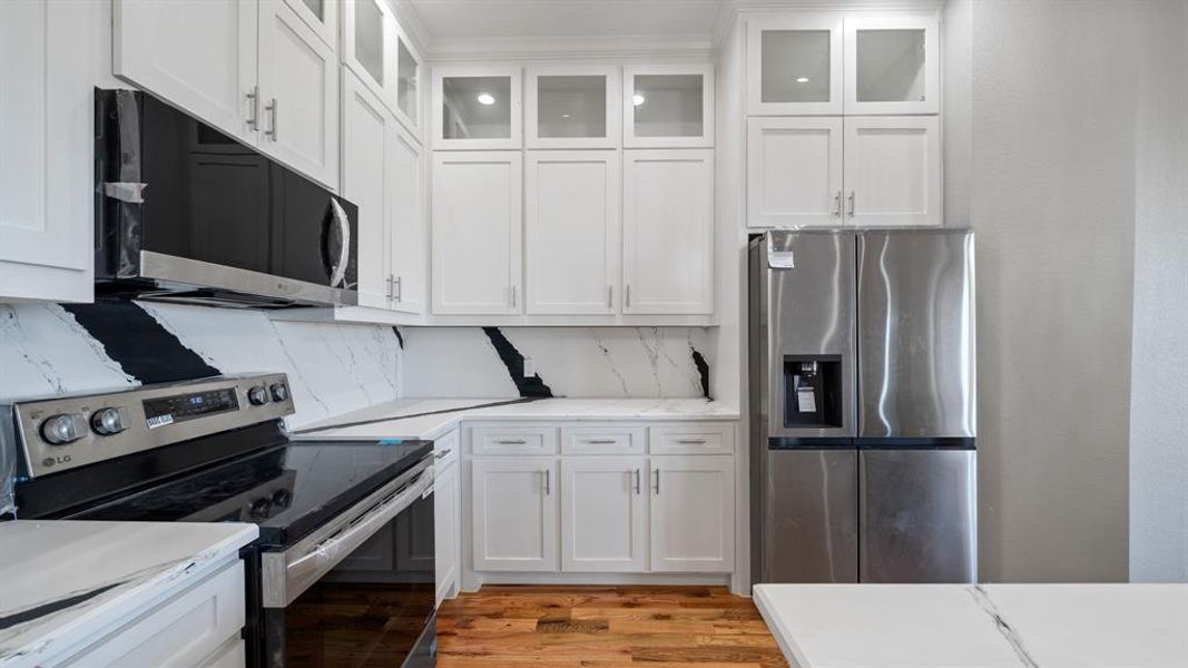 Kitchen featuring stainless steel appliances, decorative backsplash, and white cabinets