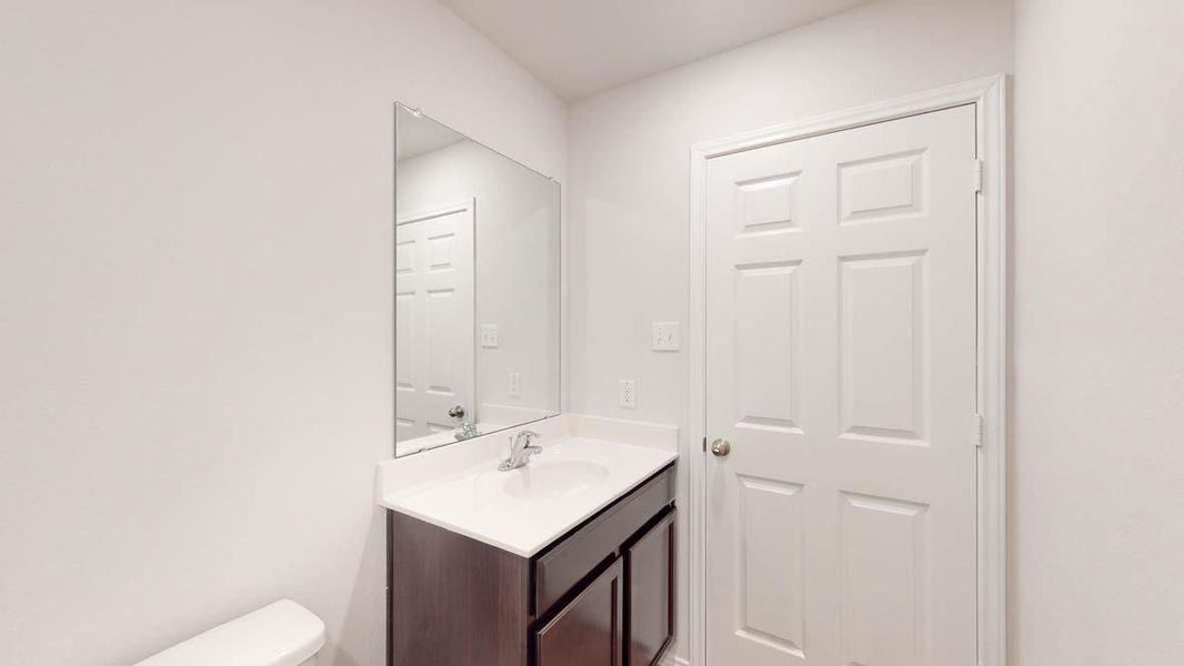 Bathroom featuring a dark wood-finish vanity with a white countertop and integrated sink, a rectangular wall-mounted mirror, and a white paneled door