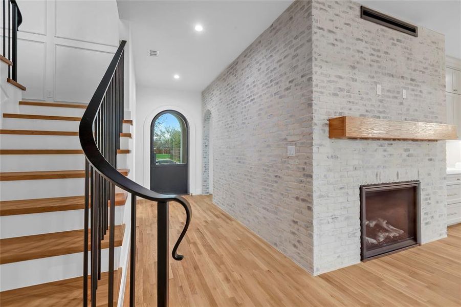 Stairs with brick wall, a brick fireplace, wood finished floors, and recessed lighting