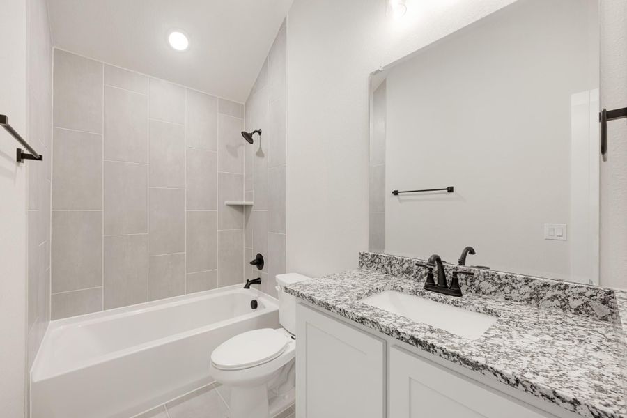 Bathroom with granite vanity, white tub-shower combo, gray tile surround, and black fixtures