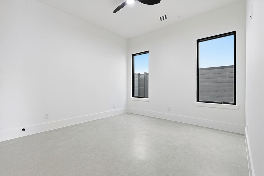 This bedroom features high ceilings, large-format tile flooring, and oversized black-framed windows that maximize natural light.