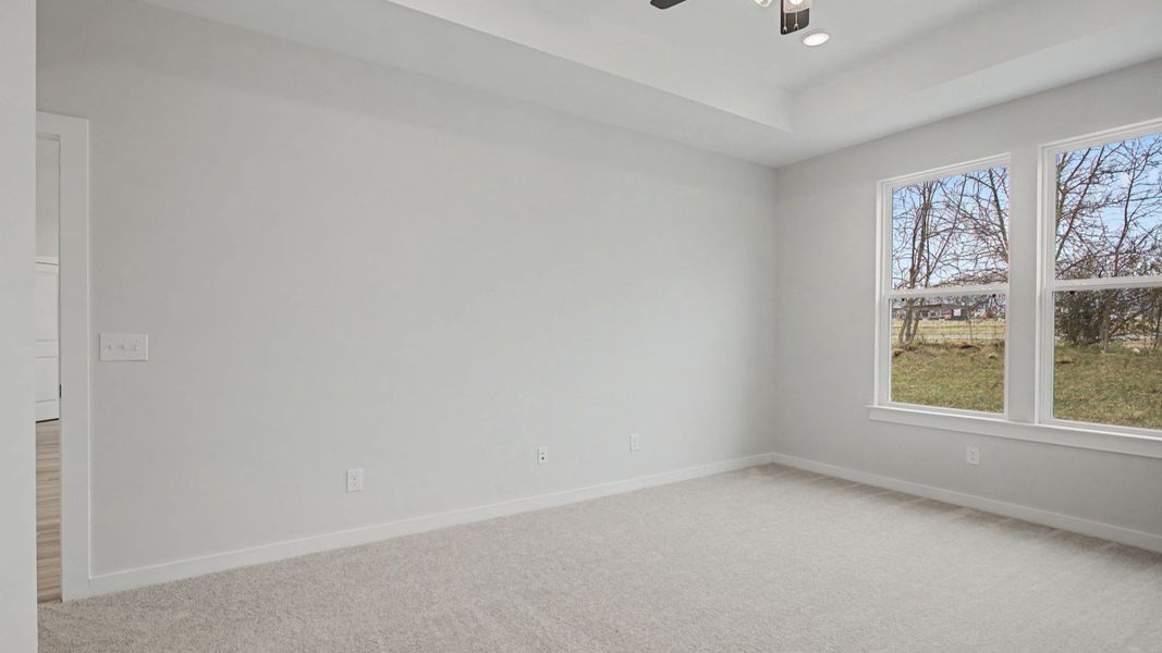 Primary bedroom with tray ceiling and ceiling fan, and door to living area