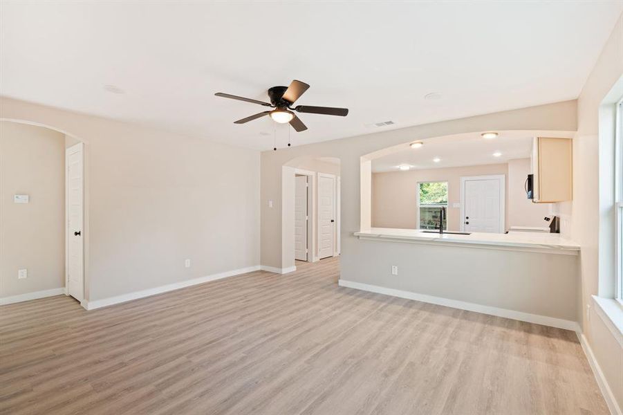 Unfurnished living room with arched walkways, light wood finished floors, a ceiling fan, and recessed lighting