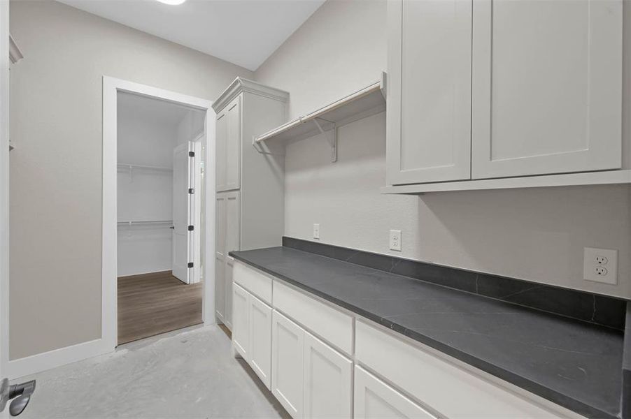 The laundry room, from the hallway, that connects to the primary closet too with upper and bottom cabinets for extra storage.