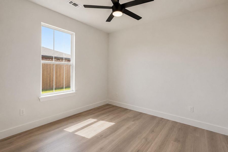 3rd bedroom A quiet bedroom offering light wood flooring, a window overlooking a privacy fence, and a modern ceiling fan.