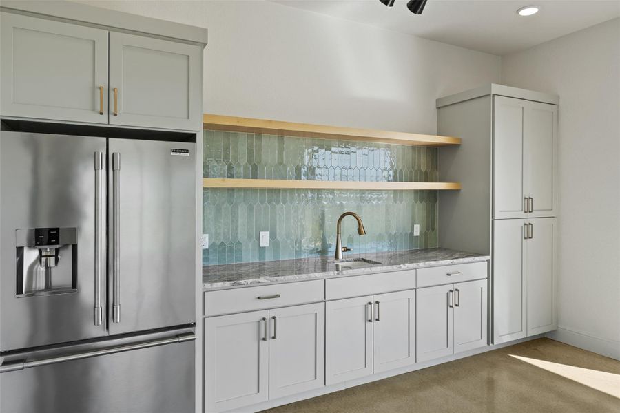 Kitchen featuring open shelves, light stone counters, light carpet, high quality fridge, and a sink