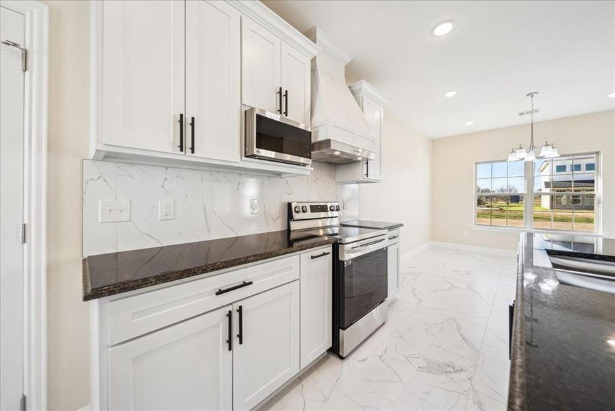 Kitchen with white cabinetry, hanging light fixtures, stainless steel appliances, an inviting chandelier, and custom range hood