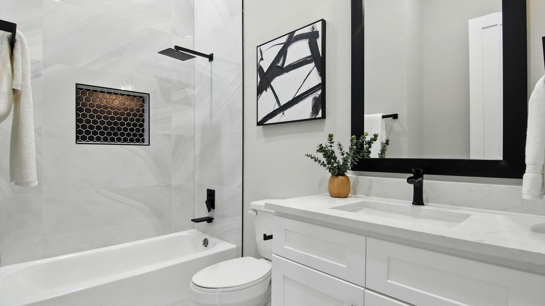 This modern full bathroom exudes elegance with its marble-look tile surround, matte black fixtures, and striking hexagon tile accent niche. The white vanity with quartz countertop and framed mirror provide a clean, timeless aesthetic. This modern full bathroom exudes elegance with its marble-look tile surround, matte black fixtures, and striking hexagon tile accent niche. The white vanity with quartz countertop and framed mirror provide a clean, timeless aesthetic.