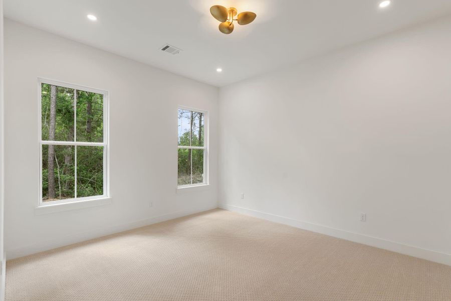 Spacious guest suite with large windows that bring in natural light and neighborhood views. Neutral tones and wide-plank wood flooring create a clean, inviting feel, while recessed lighting and a modern ceiling fixture add a polished touch. Generous wall space allows for flexible furniture placement, making this room comfortable and private for visitors.