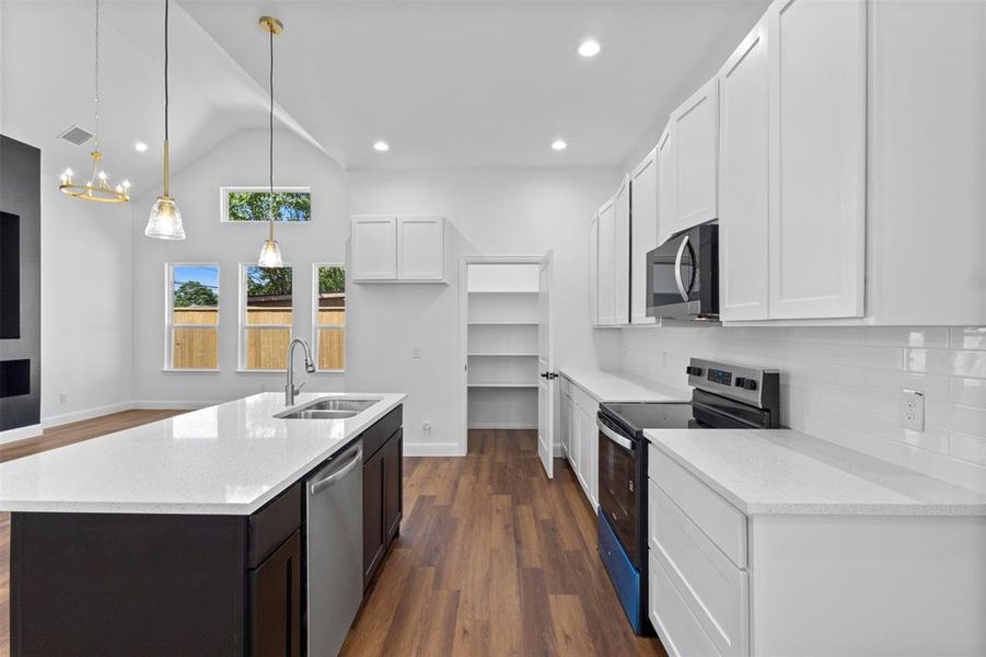 Kitchen with appliances with stainless steel finishes, dark wood finished floors, decorative backsplash, white cabinetry, and lofted ceiling