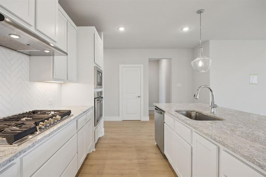 Kitchen featuring white cabinets, light wood-type flooring, under cabinet range hood, light stone counters, and stainless steel appliances