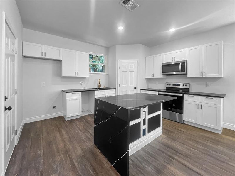 Kitchen featuring white cabinets, appliances with stainless steel finishes, a center island, and dark hardwood / wood-style floors