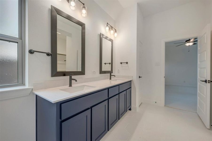 Dual vanity featuring navy cabinetry, stone countertop, matte black fixtures, and framed mirrors