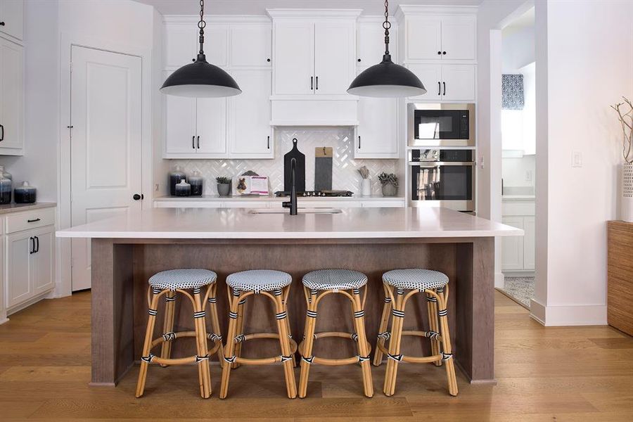 Kitchen featuring white cabinetry, stainless steel appliances, a center island with sink, tasteful backsplash, and decorative light fixtures