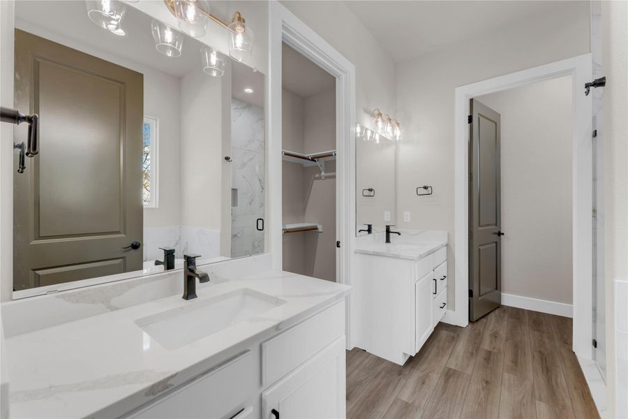 Bathroom with a marble finish shower, two vanities, and light wood-style flooring