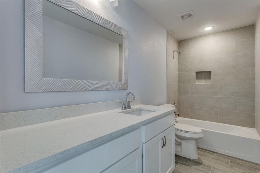 Full bathroom with vanity, tiled shower / bath combo, and toilet