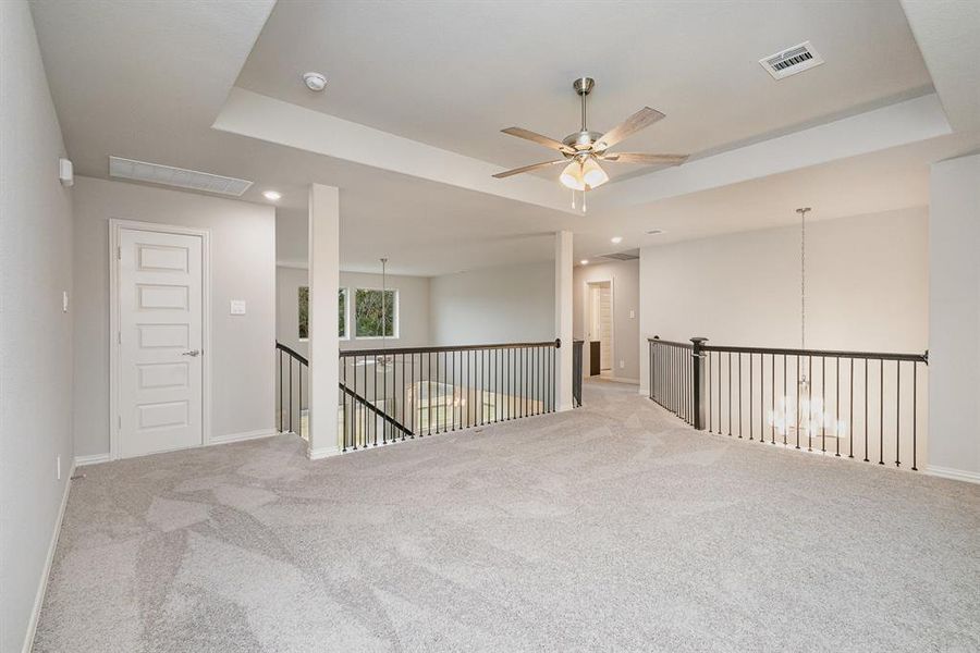 Empty room featuring ceiling fan, light colored carpet, and a tray ceiling