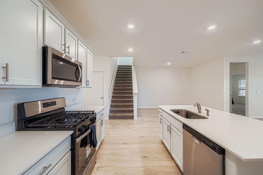 Kitchen with appliances with stainless steel finishes, light wood-type flooring, an island with sink, white cabinets, and recessed lighting