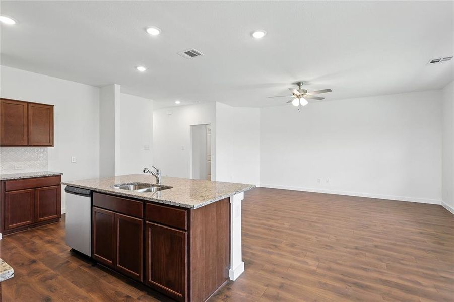 Kitchen with stainless steel dishwasher, a ceiling fan, dark wood-style floors, an island with sink, and backsplash Kitchen with stainless steel dishwasher, a ceiling fan, dark wood-style floors, an island with sink, and backsplash