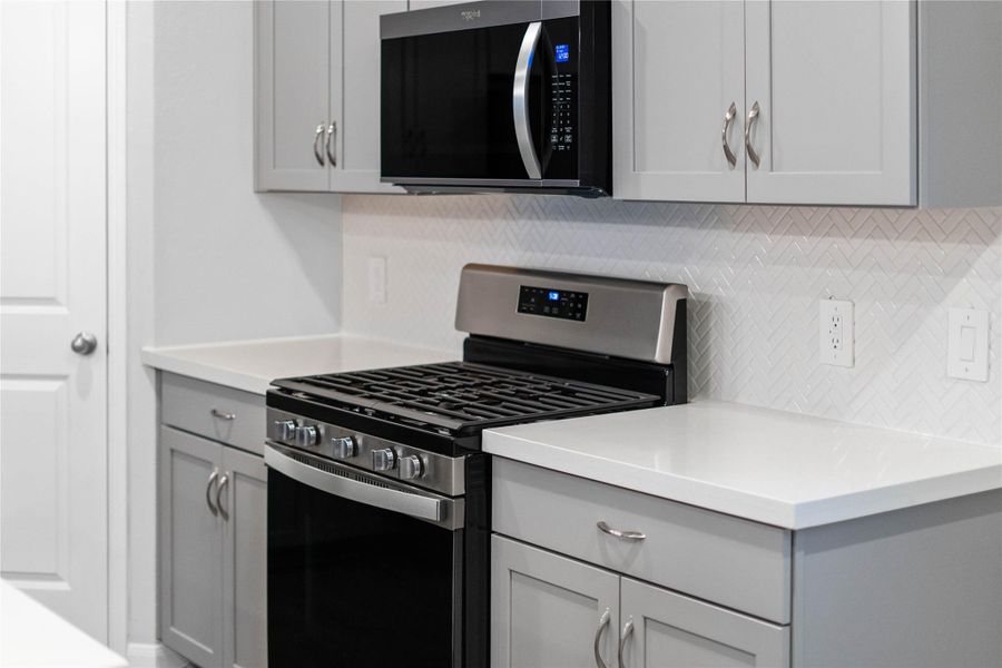 Showcased here is a Whirlpool gas range featuring a versatile center oval burner, paired with a steam microwave equipped with sensor cooking—all framed by an elegant tile backsplash.