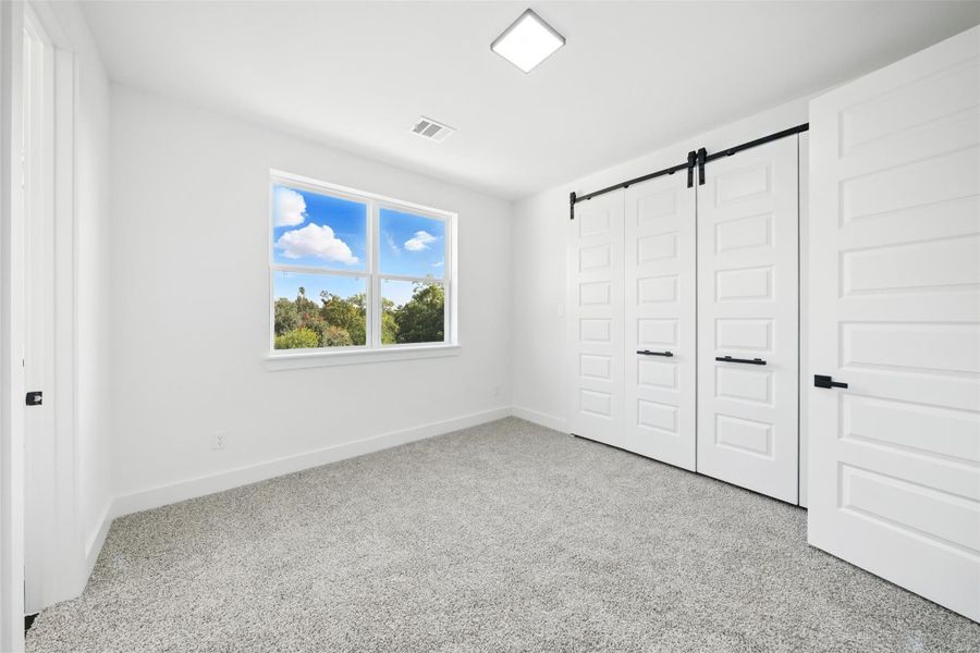 Light-filled bedroom with a clean, modern design, featuring plush carpet, a large window with scenic views, and a spacious layout. Includes a stylish sliding barn door closet with ample storage, combining functionality with contemporary design. Light-filled bedroom with a clean, modern design, featuring plush carpet, a large window with scenic views, and a spacious layout. Includes a stylish sliding barn door closet with ample storage, combining functionality with contemporary design.