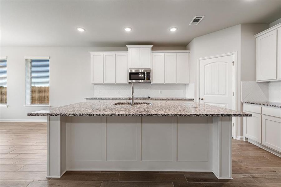 Kitchen with wood tiled floors, white cabinetry, light stone countertops, tasteful backsplash, and stainless steel microwave Kitchen with wood tiled floors, white cabinetry, light stone countertops, tasteful backsplash, and stainless steel microwave