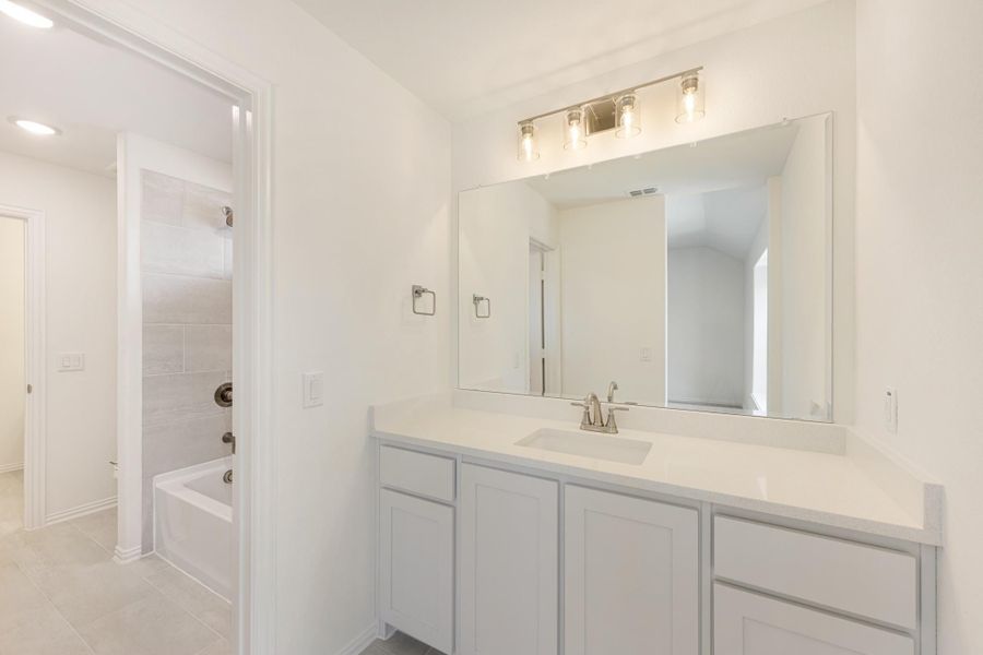 Bathroom with white vanity, large mirror, and separate tub and shower area visible through doorway Bathroom with white vanity, large mirror, and separate tub and shower area visible through doorway