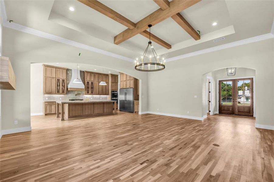 Unfurnished living room with arched walkways, beam ceiling, a chandelier, recessed lighting, and light wood-style floors