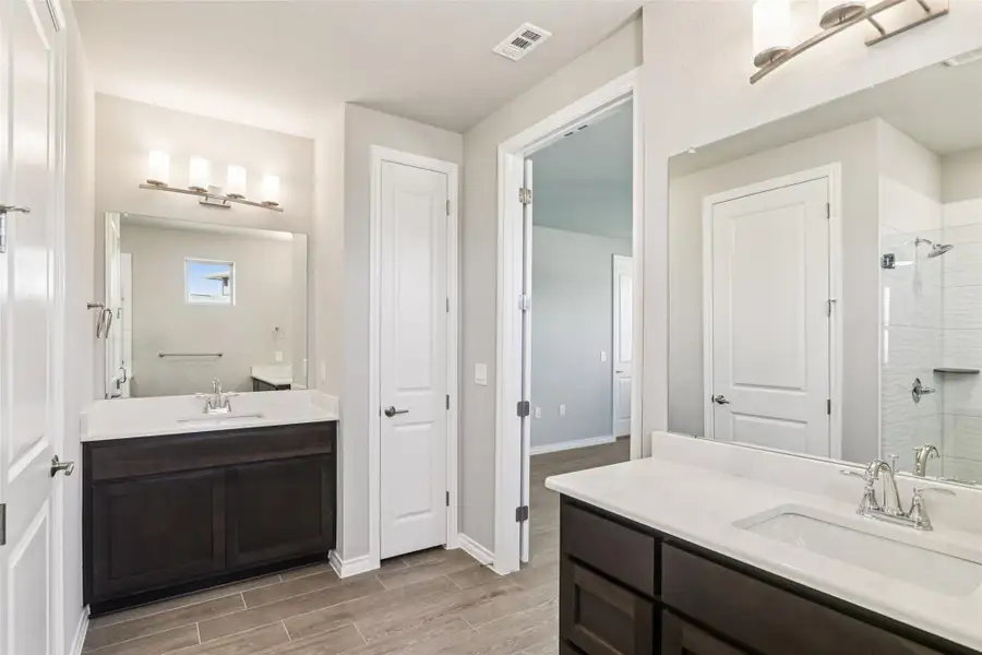 Full bathroom with a stall shower, two vanities, and wood finished floors