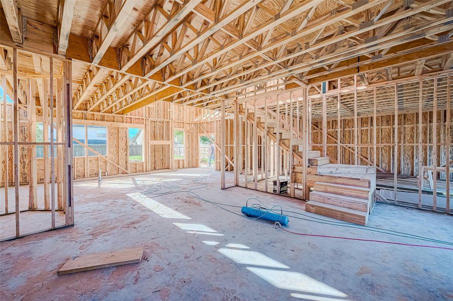 This photo shows the interior of a house under construction, featuring exposed wooden framing, open spaces, and large window openings. There's a staircase structure in place, and natural light illuminates the area. Ideal for buyers interested in customizing their new home.