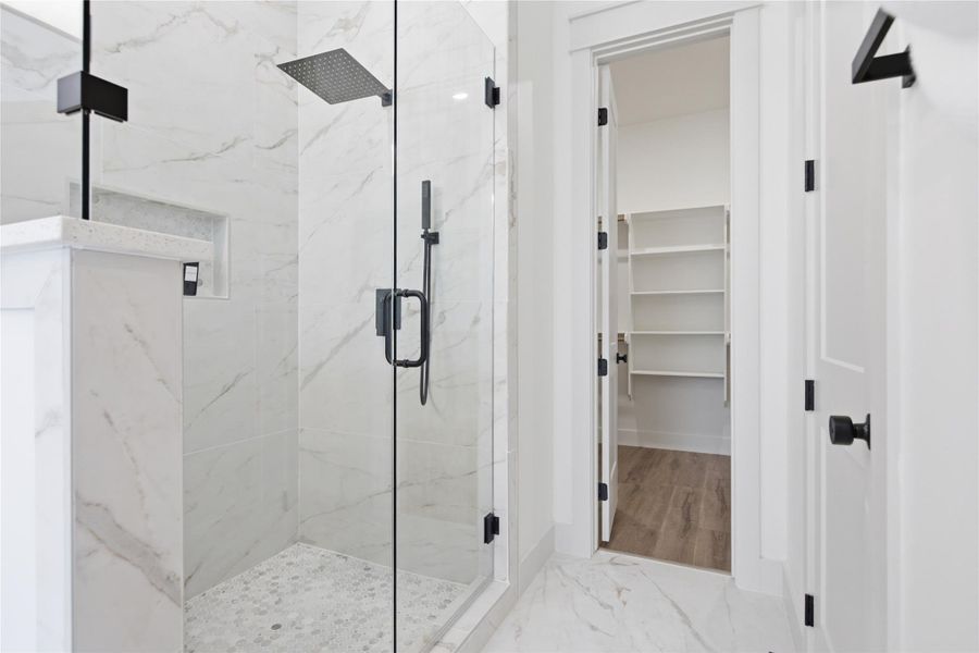 A spacious, glass-enclosed shower with contrasting dark fixtures anchors this pristine bathroom, leading to a generously sized walk-in closet. A spacious, glass-enclosed shower with contrasting dark fixtures anchors this pristine bathroom, leading to a generously sized walk-in closet.