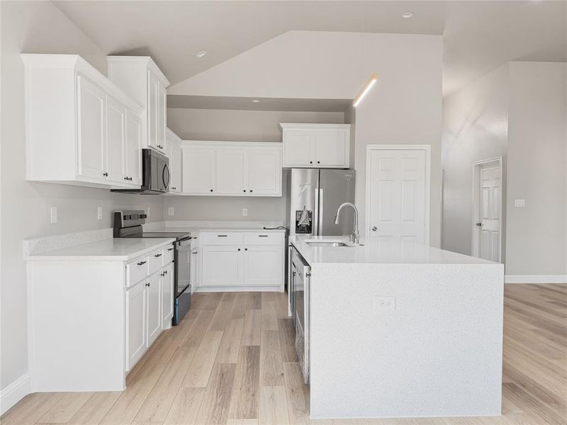 Kitchen with stainless steel appliances, light wood-style flooring, light stone counters, white cabinetry, and a center island with sink