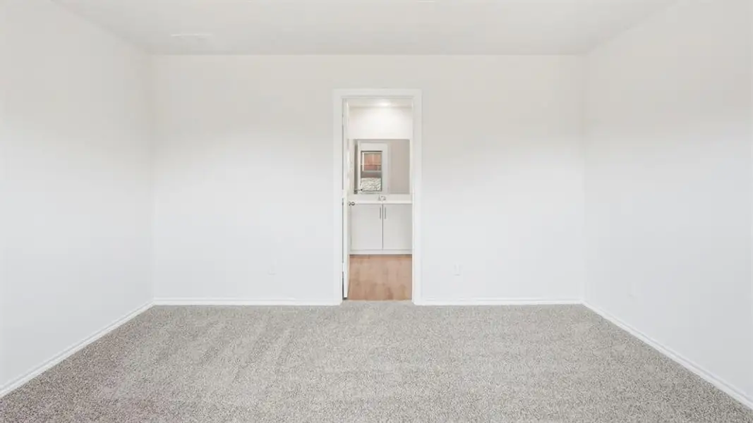 The room features light gray carpet and white walls, with a doorway leading to a room with wood flooring and a vanity with white cabinetry