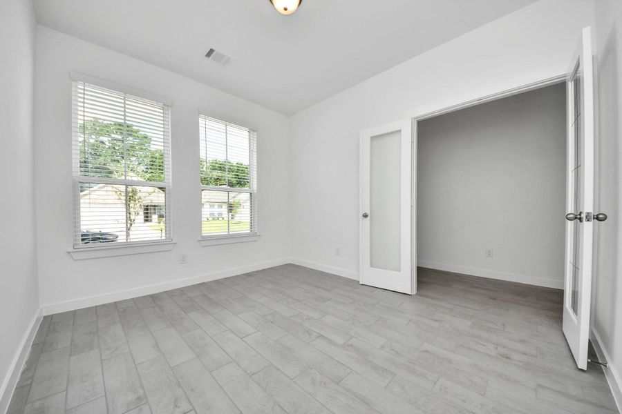 Experience the perfect blend of sophistication and warmth in this home office, boasting elegant wood-look tile flooring and flooded with natural light from expansive windows and French doors. Sample photo of completed home with similar floor plan. Actual colors and selections may vary.