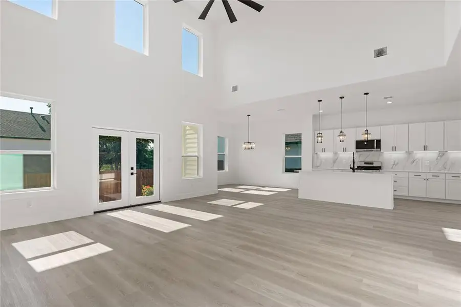 Unfurnished living room featuring french doors, light wood finished floors, a ceiling fan, and a towering ceiling